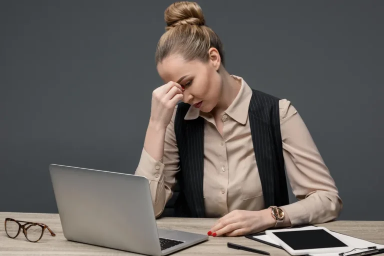 Tired businesswoman using laptop at table isolated on grey