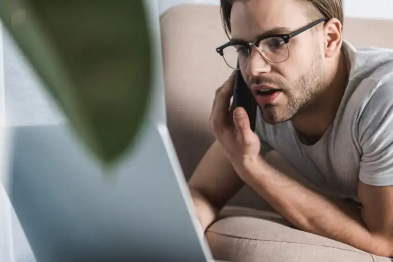 Young handsome freelancer in pajamas working with laptop on couch
